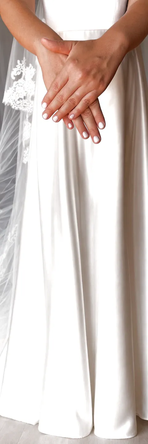 Una sposa con le mani incrociate e il velo, l'abito di raso fino all'orlo
